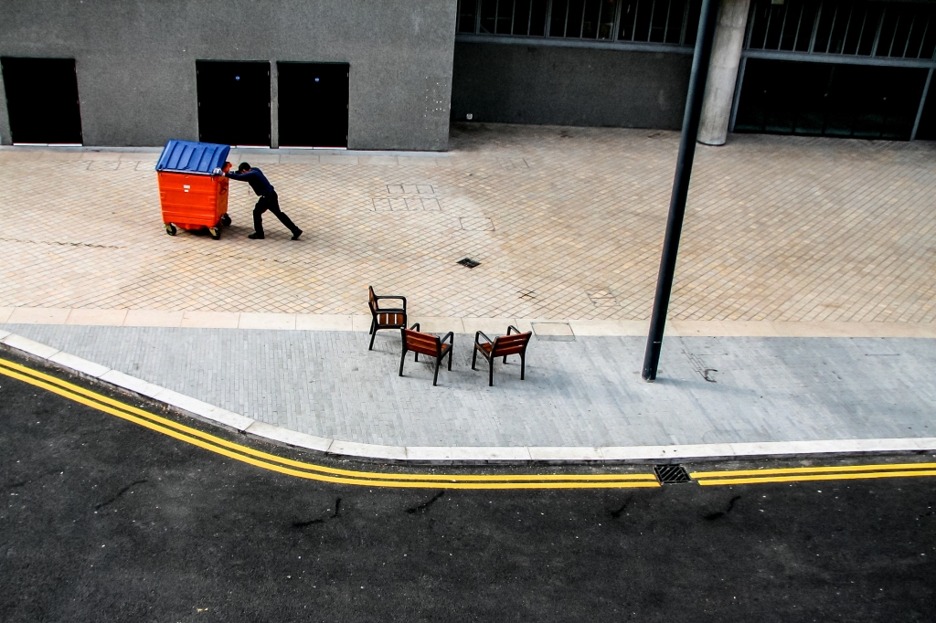 Street photography of worker pushing bin in London.