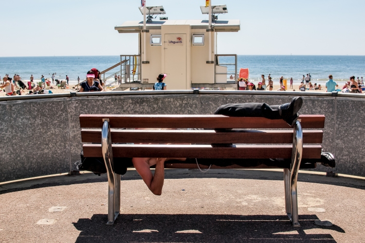 Street photography of a man twisted around a bench in Bournemouth, London