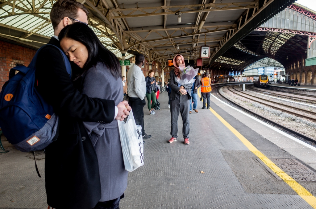 Street photography of a couple cuddling and a man with flowers, at Bristol Temple Meads station.