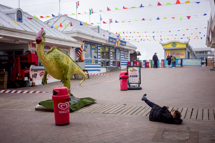 Weston-super-Mare street photography of a boy falling over by a dinosaur on the Grand Pier, by UK street photography Darren Lehane.